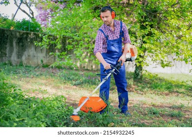 One Gardener Mowing Grass Using Brushcutter In The Garden