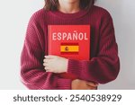 one girl schoolgirl in burgundy sweater holds red spanish language textbook with spain flag and text spanish in spanish, foreign language learning concept.