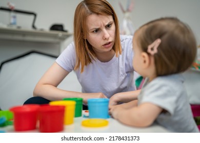 One girl small caucasian toddler child playing with colorful plasticine on the table at home with her mother woman talking angry mad childhood and growing up development concept copy space side view - Shutterstock ID 2178431373