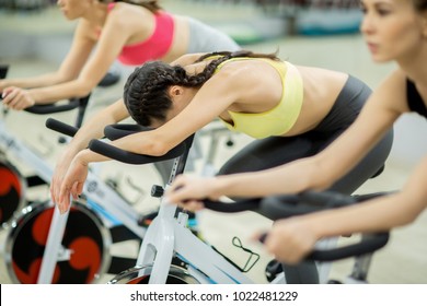 One of girls tired after workout on training bike while her two friends still exercising - Shutterstock ID 1022481229
