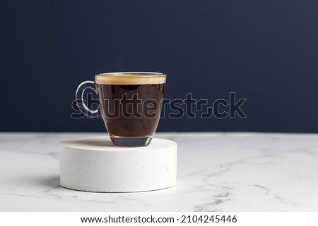 One glass coffee cup with espresso in morning on podium and white marble background. Aroma, ristretto. Mug of coffee. Blue wall