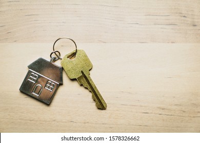 One golden house key with house shape keychain isolated on wood background - Powered by Shutterstock