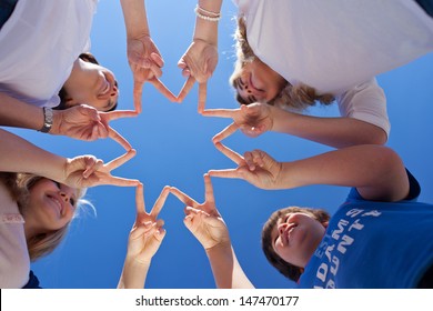 One good successful team of young teenage children forming a star with their fingers touching to the form the points against a clear blue sky, conceptual of cooperation and teamwork