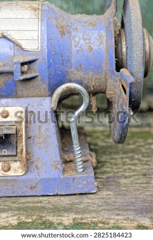 one gray long machine screw is screwed into a blue iron grinder in a wooden table