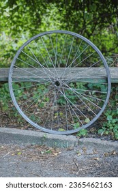 one gray metal rim of a bicycle stake with spokes stands on the asphalt near a wooden table on a summer street - Shutterstock ID 2365462163