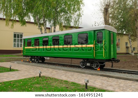 One green carriage of passenger train on pedestal, railway transport monument. Small size narrow-gauge wagon of old Soviet epoch. Railroad transporting scenery