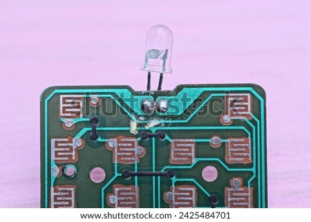 one green old plastic microcircuit with small LED bulb with lead soldering lies on a pink table