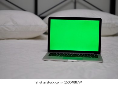 One Green Screen Laptop Computer On Bed. Blur White Quilt And Pillows Background