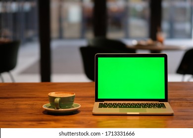 One Green Screen Laptop Computer On Wooden Table In Cafe. Blur Background