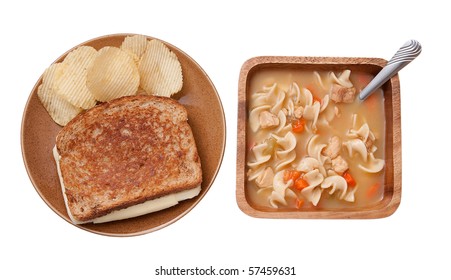 One Grilled Cheese Sandwich With Plain Chips And A Bowl Of Chicken Noodle Soup. Traditional Homestyle Food On Rustic Dishes