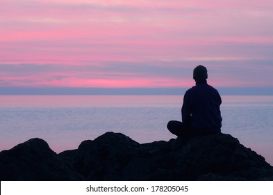 One guy sits on a rock by the sea and looking at pink sunset - Powered by Shutterstock