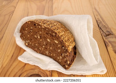 One half of rye multigrain bread with linen white napkin on wooden table, macro.
