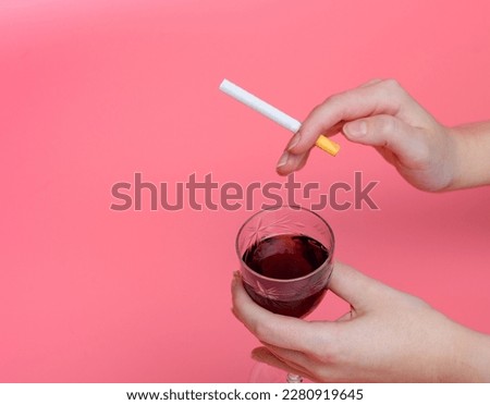 In one hand a cigarette in the other a glass with wine on a pink background