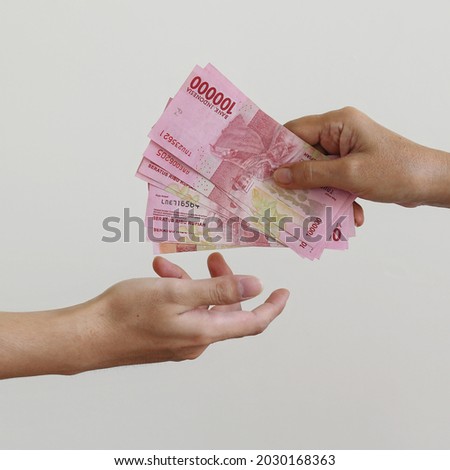 One hand delivering some amount of money to another hand symbolizing cash payment. Pembayaran cash dengan Rupiah