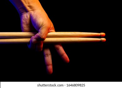 one hand holding wooden drum stick and showing two fingers with dark background, red and blue rim light, keep fighting drummer and musician concept