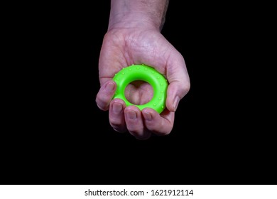 one hand holds a green rubber ring to strengthen the muscles against a black background