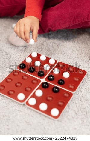 One hand hovers over the game board, holding black and white marbles. Child is ready to place the marbles, carefully thinking about the next move. 