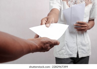 One hand passes a white envelope filled with money or bills into the other. the concept of giving allowances for Eid al-Fitr - Shutterstock ID 2282967399
