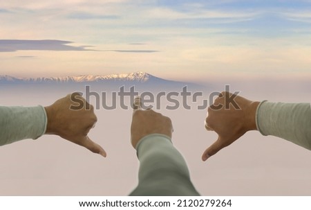 One hand pointing up, others pointing down on mountain peak background. Concept of faith, motivation, foresight, goal.  