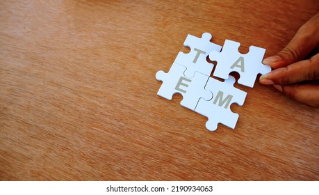 One Hand Put White Jigsaw Puzzle Together. With Wording Of Team. Concep Pf Team Work And Team Player.