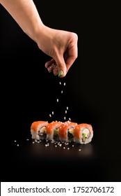 One hand sprinkling sushi on the black matte background