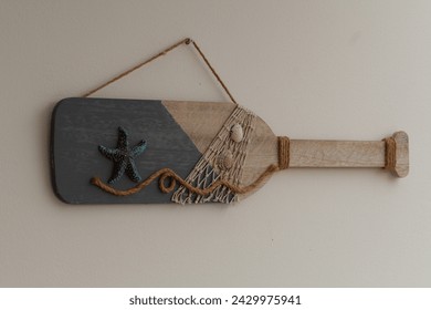One hanging wooden beach decoration shaped as a floating bottle with a blue starfish and seashells in a plain white wall background