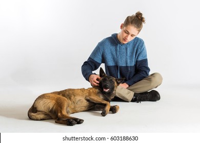 One Happy Calm Young Male Belgian Malinois Puppy Laying Down On Floor While Being Pet By A Teenage Boy. Teen Boy Giving Loving Attention To His Dog. 