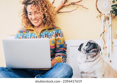 One happy woman using laptop outdoor at home sitting near her best friend dog pug and enjoying technology and friendship. Cheerful attractive female work on computer in wireless connection. Leisure - Shutterstock ID 2396417619