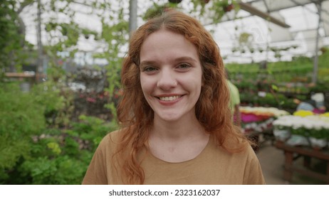 One happy young RedHead woman smiling at camera standing inside Flower Shop in Natural Green Environment. A female 30s person portrait face close-up - Powered by Shutterstock