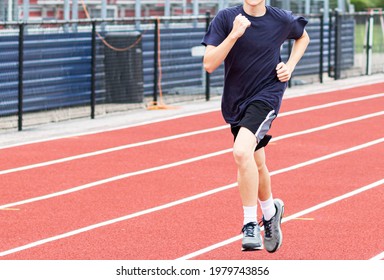 One High School Boy Running On A Red Track With The Bleachers In The Background.