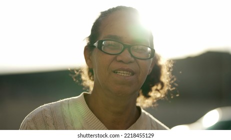 One Hispanic Senior Woman Standing In Sunlight. Older South American Mature Female Person Standing Outdoors Looking At Camera