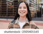 One hispanic woman looking at camera with friendly expression. Close up individual portrait of a latina female smiling, standing outside and staring front. Headshot of a pleased teenage latin girl