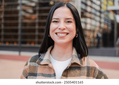 One hispanic woman looking at camera with friendly expression. Close up individual portrait of a latina female smiling, standing outside and staring front. Headshot of a pleased teenage latin girl - Powered by Shutterstock