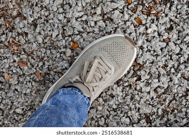 One human foot with brown shoe and blue denim pants standing on horizontal ratio small rocks pebbles ground background. - Powered by Shutterstock