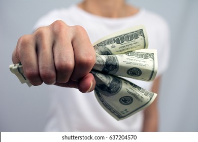 one hundred dollar bills crumpled in hand young woman white t-shirt grey neutral blurred background