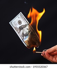 One hundred dollars are burning from a match on a black background.