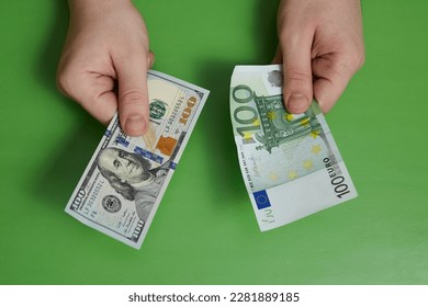 One hundred dollars in one hand and one hundred euros in the other on a green background. Cash currency exchange. - Shutterstock ID 2281889185