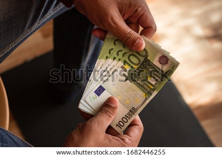 one hundred euro banknotes in working hard palms of man against black and brown background