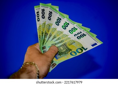 One hundred euro bills in a man's hand with a gold bracelet. Plain background. Cash in hand. European cash. 