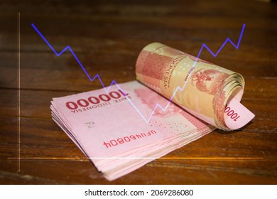 One Hundred Thousand Rupiah Bill With A Blue Line Chart Going Up And Down On A Brown Wooden Table Background