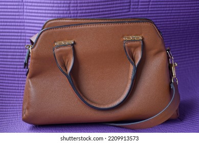 One Large Brown Leather Bag Stands On A Purple Table