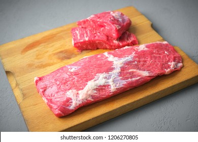 one large piece of beef brisket on a wooden butcher's Board and two small steaks