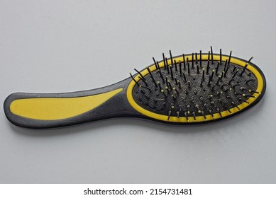 One Large Plastic Black Yellow Dirty Hairbrush Lies On A White Table