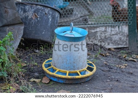 one large plastic colored dirty chicken drinker stands on gray ground outdoors in a farm