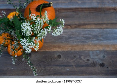 One large and several small pumpkins , with bouquet of small white flowers. In upper right corner of  wooden background. 