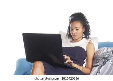 One Latin American Young  Woman Neutral Expression Sitting With Crossed Legs On Sofa Or Couch Using Laptop With White Background For Copy.woman With Laptop On Legs
