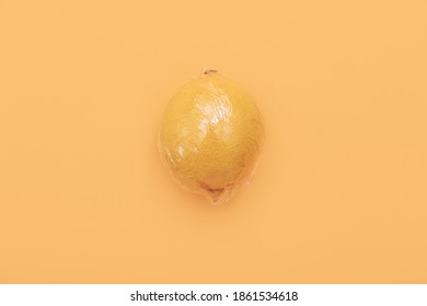 One Lemon In Wrap Polyethylene Plastic On Orange Background. Minimal Enviromental Concept. Flat Flat, Top View