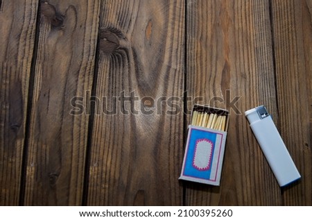One lighter will replace a box of matches. A white plastic lighter and a matchbox lie on a wooden surface. Matches and lighters, campfire accessories