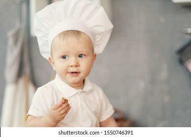 one little boy in hat of chef in kitchen sitting on the table and eat 