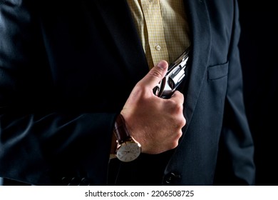 One Male Spy In A Professional Tuxedo Holds A Revolver Pistol Before The Start Of A Film Shoot. Portrait Silhouette In The Studio. Isolated Black Background. Male Actor With A Gun